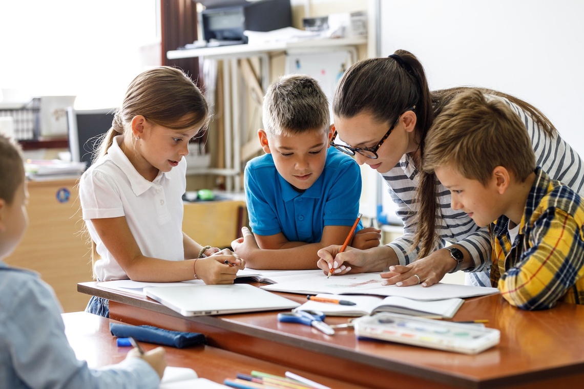Kinder arbeiten mit Lehrerin am Tisch an einer Aufgabe 