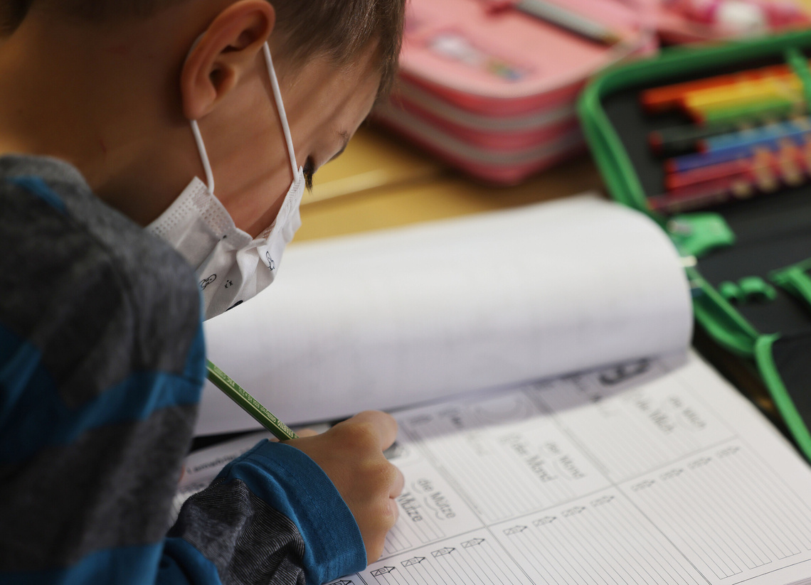 Schulkinder mit Maske füllt Hausaufgaben aus