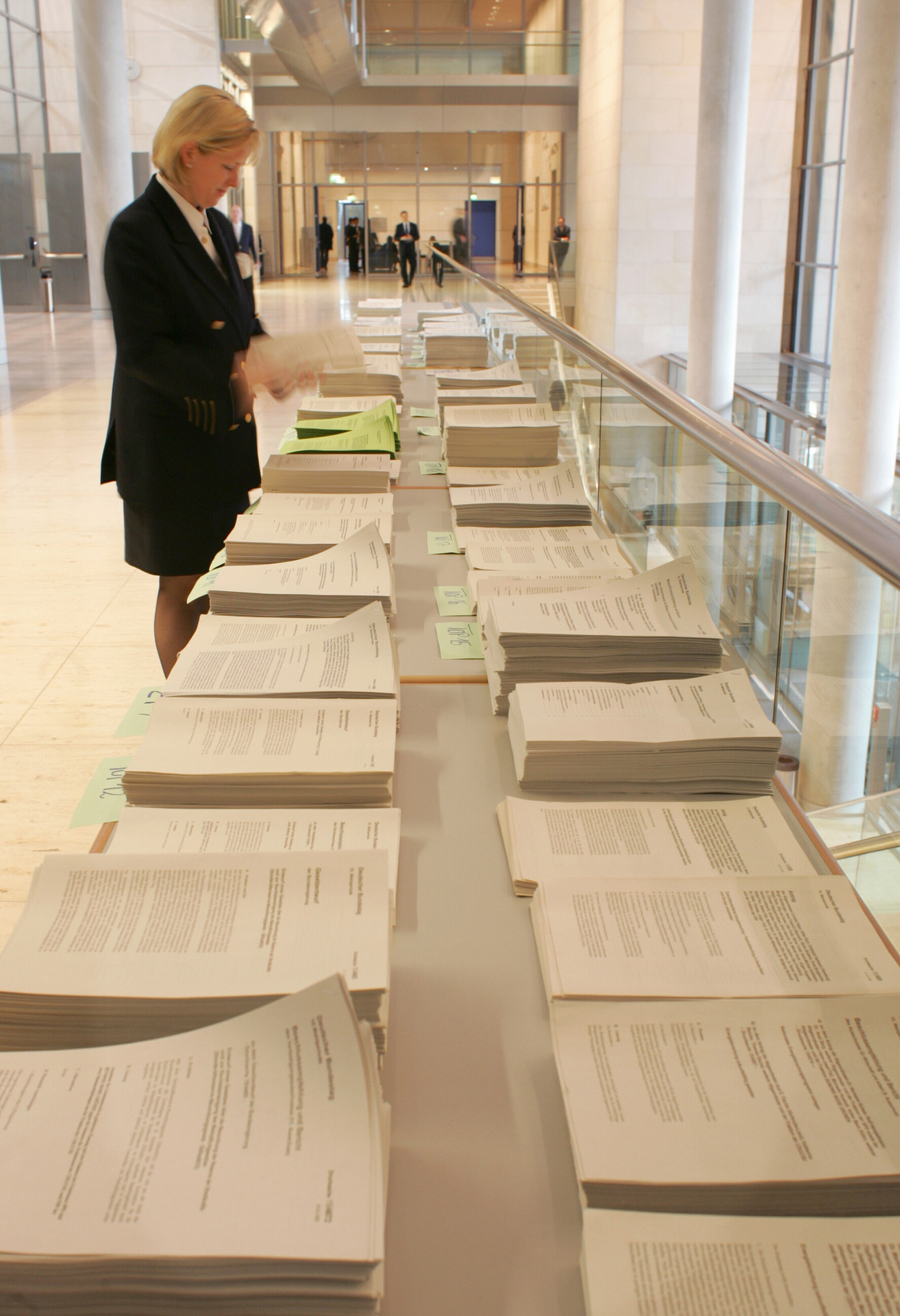 Papierstapel mit Anträgen und Frau in schwarzem Blazer und Rock