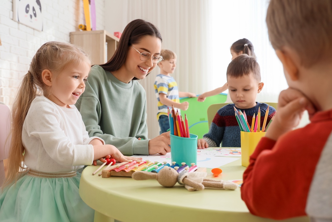 Erzieherin sitzt mit Kindern am Tisch.
