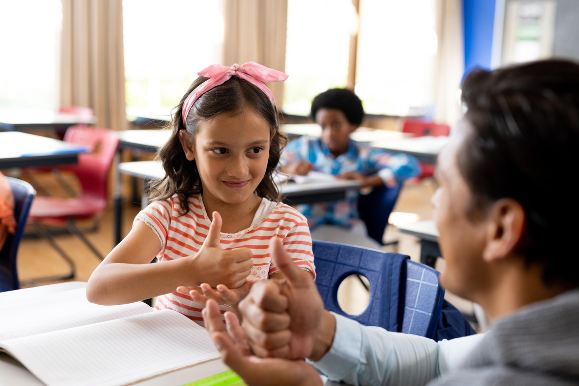 Zwei Personen unterhalten sich in einem Klassenzimmer in Gebärdensprache.