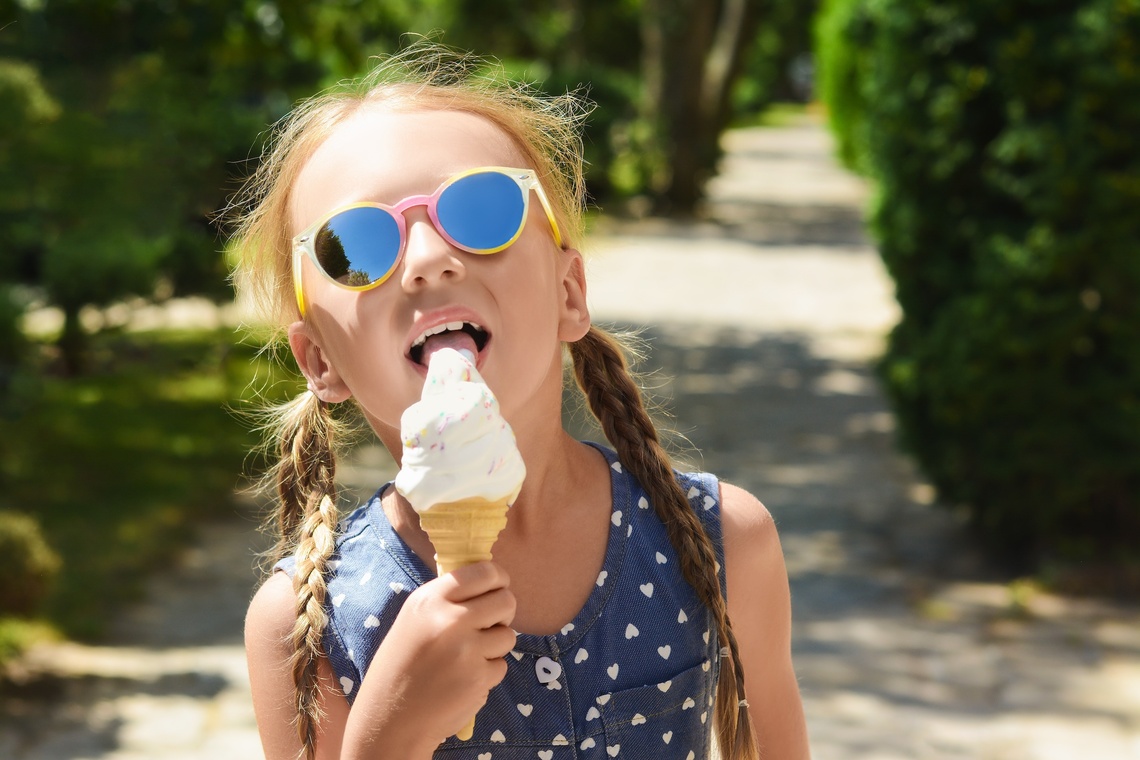 Kind mit Sonnenbrille isst ein Eis.