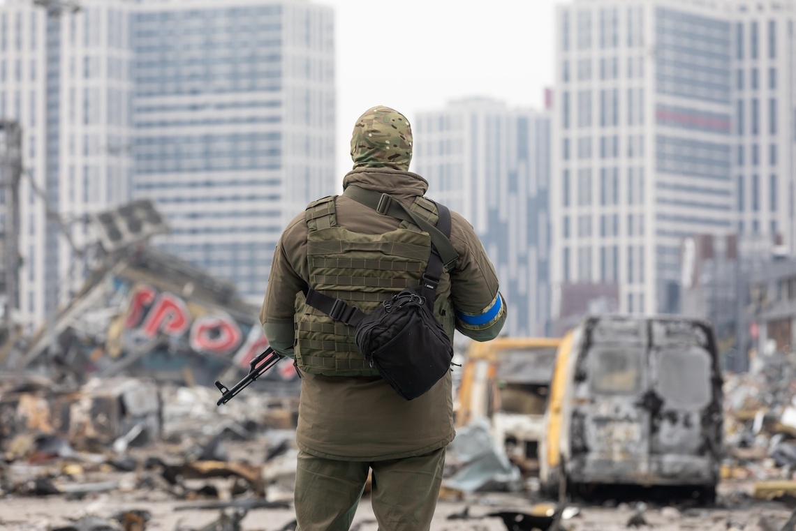 Ein ukrainischer Soldat steht mit einem Waffe in der Hand vor einem zerstörten Gebäude in Kiew