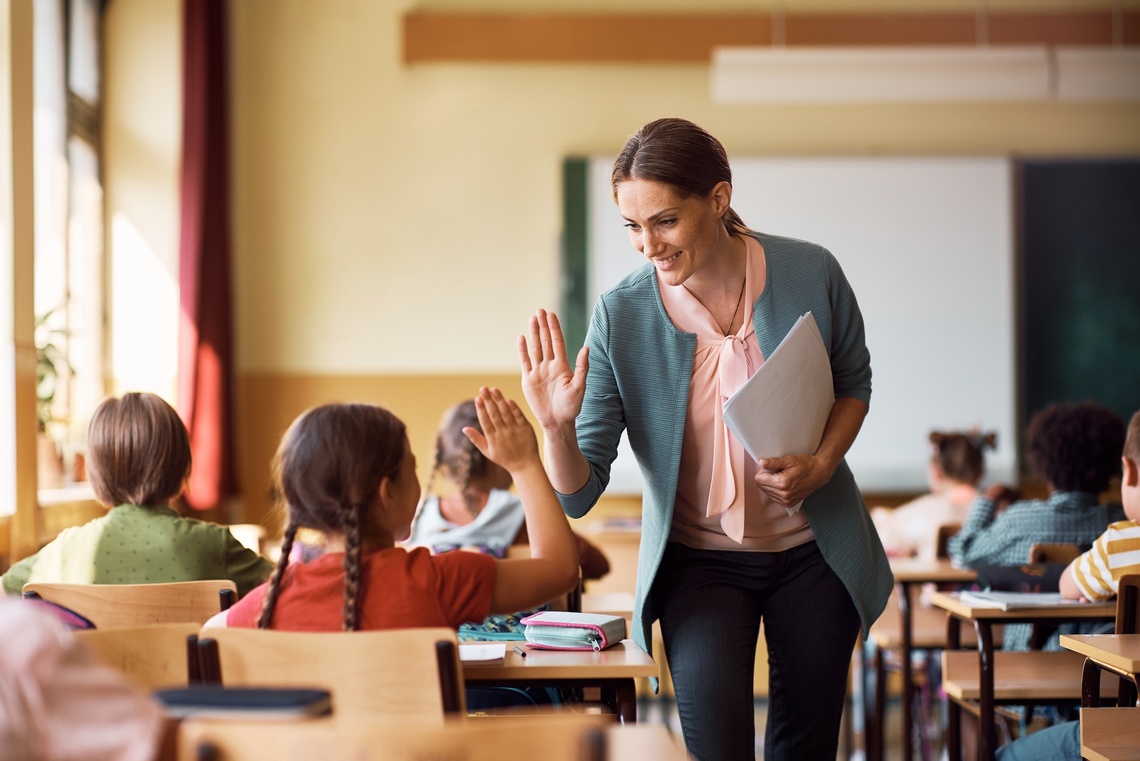 Eine Lehrerin und ein Mädchen geben sich ein Highfive im Klassenzimmer.