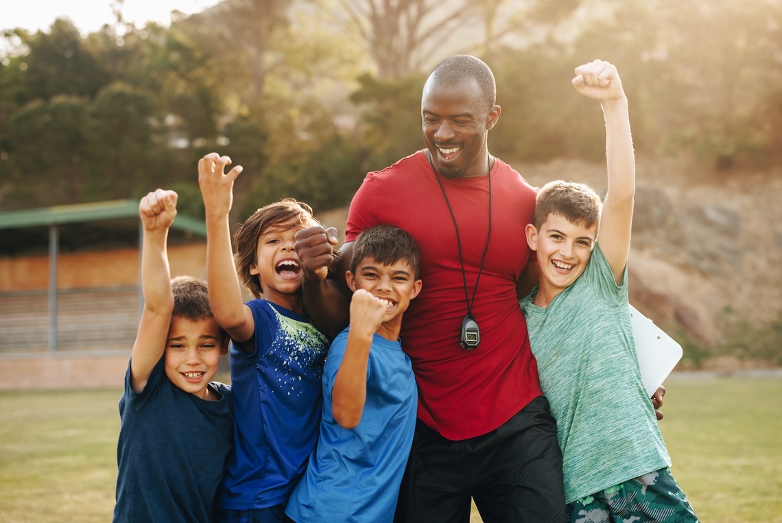 Schulkinder feiern mit ihrem Trainer auf einem Sportplatz