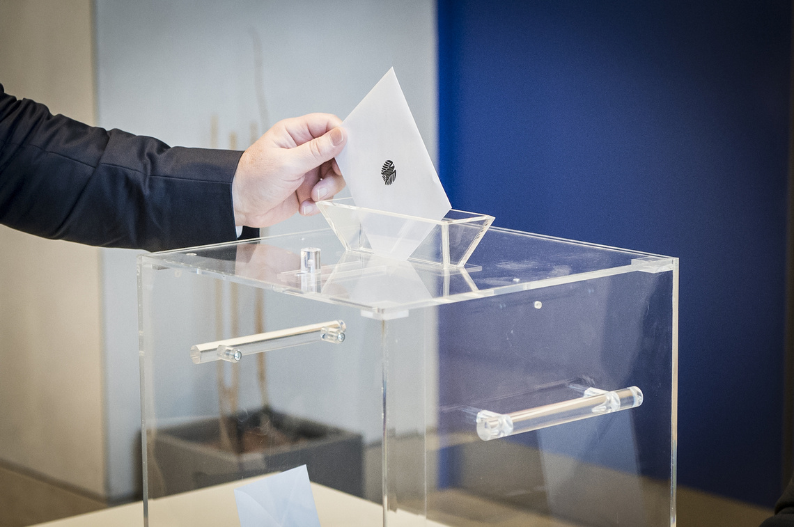Wahlurne, in die eine Hand einen Wahlzettel steckt