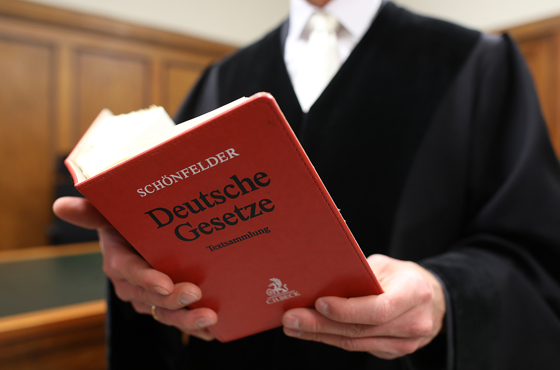 Richter hält ein Buch mit Aufschrift "Deutsche Gesetze" 