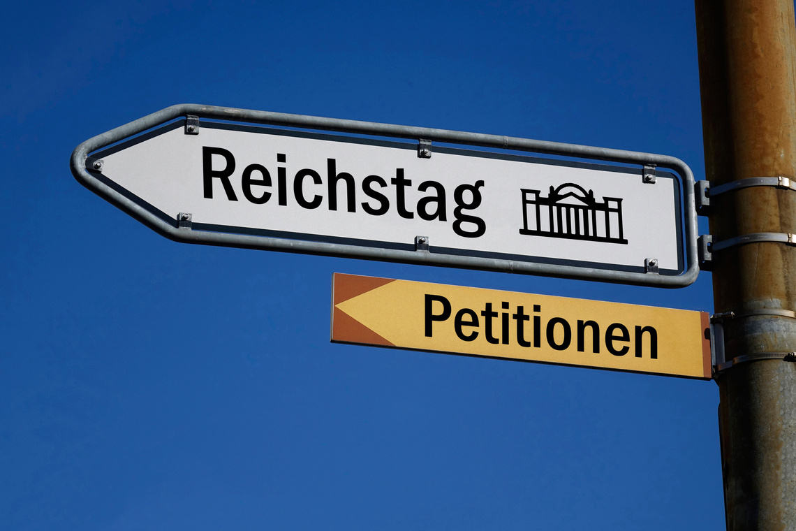 Zwei Wegweiser vor blauem Himmel: Das obere Schild zeigt zum Reichstag, das untere Schild zeigt zu den Petitionen.