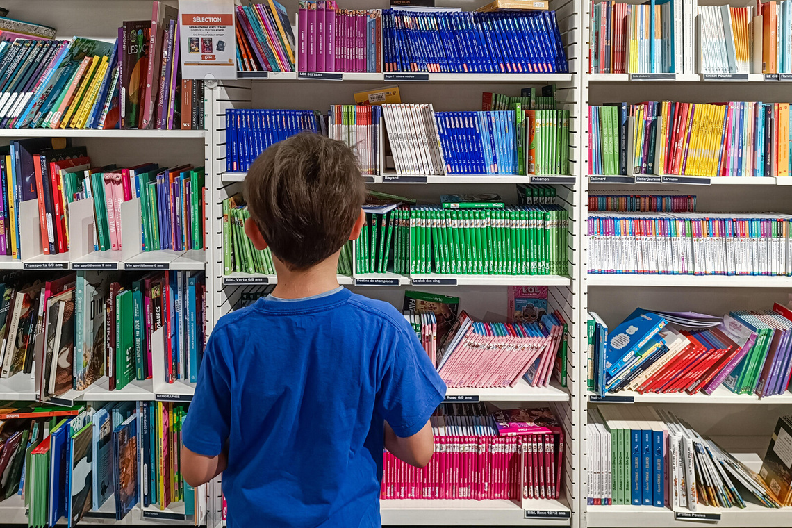 Junge in blauem T-Shirt steht vor Bücherregal