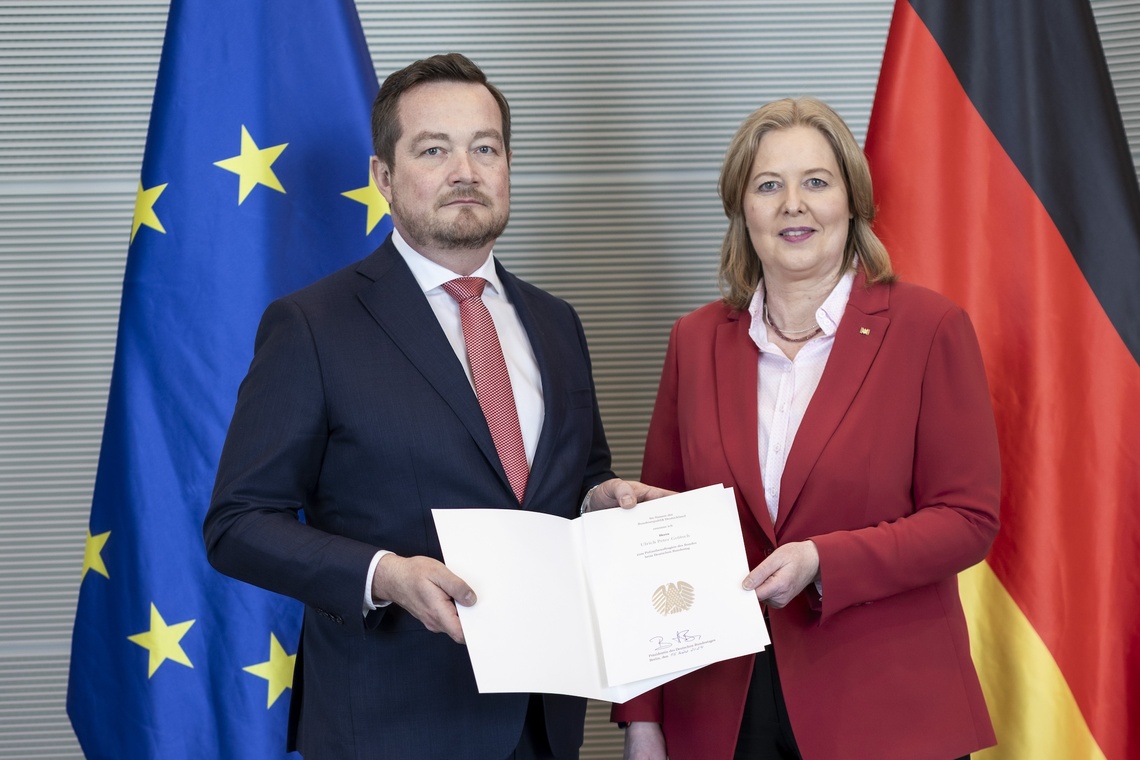 Bundestagspräsidentin Bärbel Bas überreicht Uli Grötsch die Urkunde. Im Hintergrund Europa- und Deutschland Flaggen.