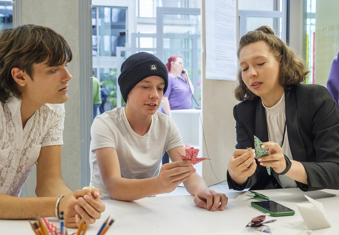 Drei Jugendliche basteln Origami Kraniche am Tisch