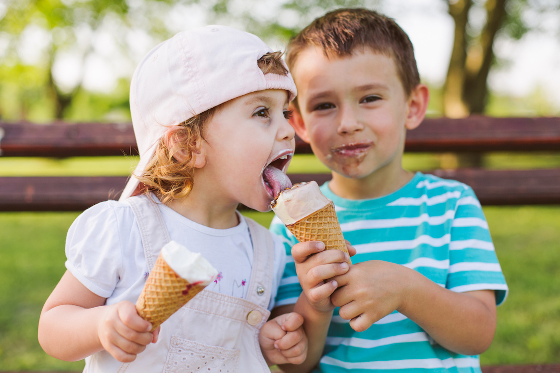 Zwei Kinder essen auf einer Bank Eis