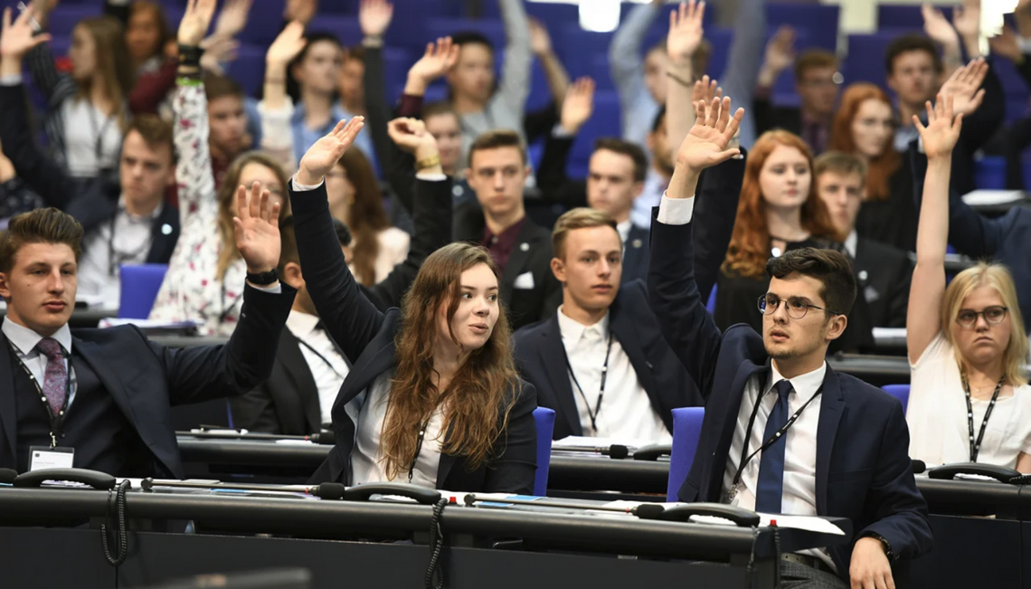 Jugendliche sitzen im Plenarsaal und stimmen ab