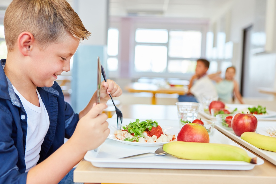 Ein Junge sitzt in der Kantine und isst Mittagessen.