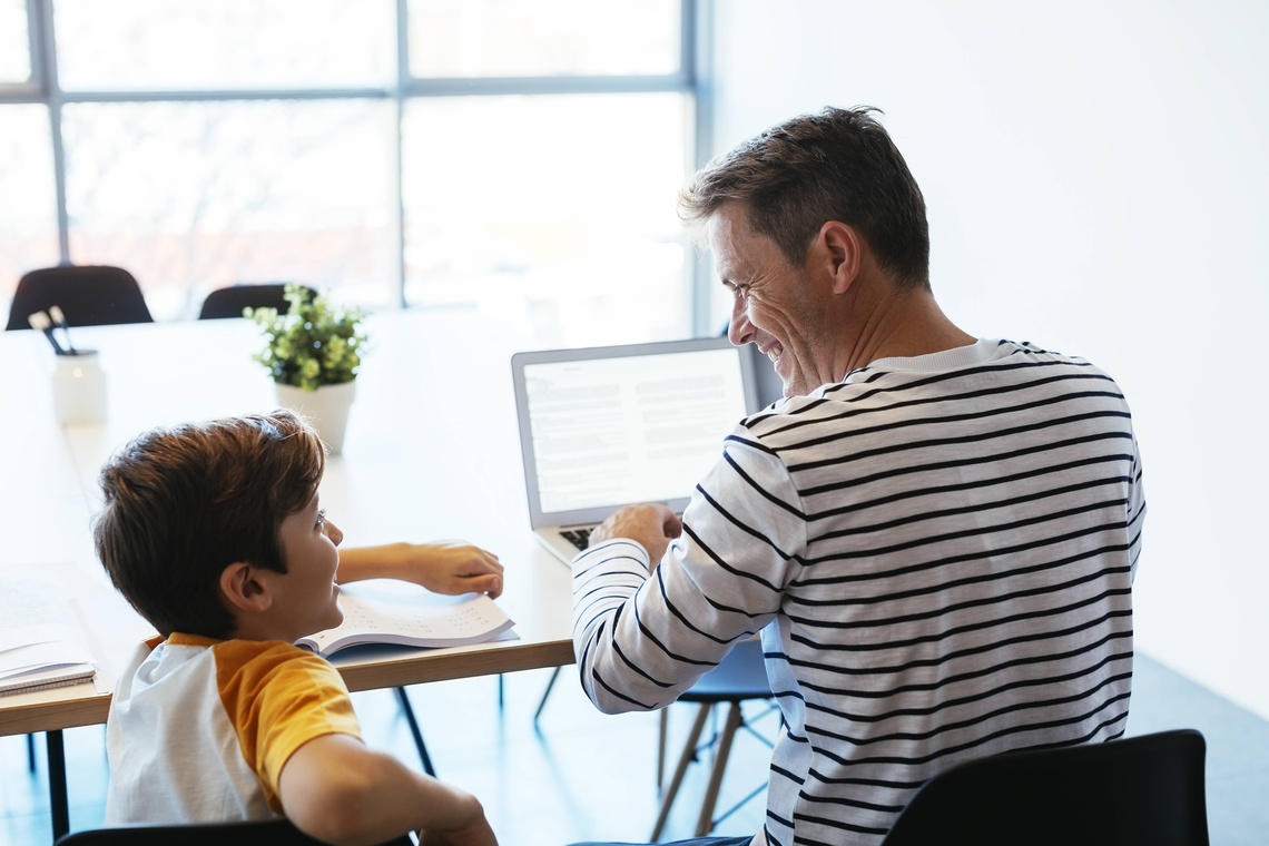 Sohn und Vater sitzen vor einem aufgeklappten Laptop.