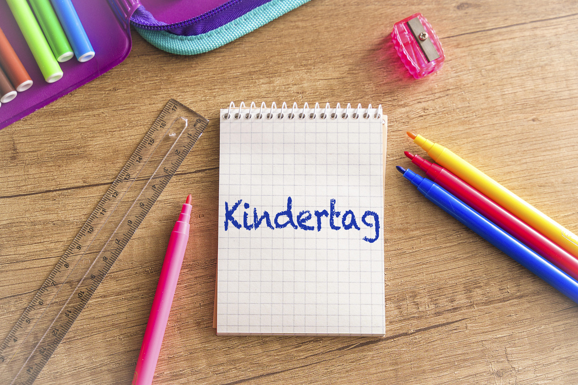 Ringblock mit dem Wort Kindertag, umgeben von bunten Stiften