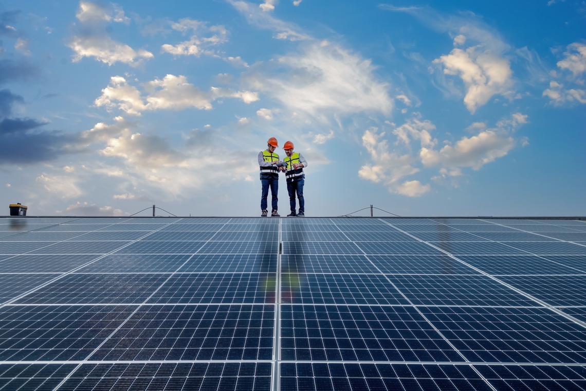 Zwei Bauarbeiter stehen auf einem Dach mit Solar Panels.