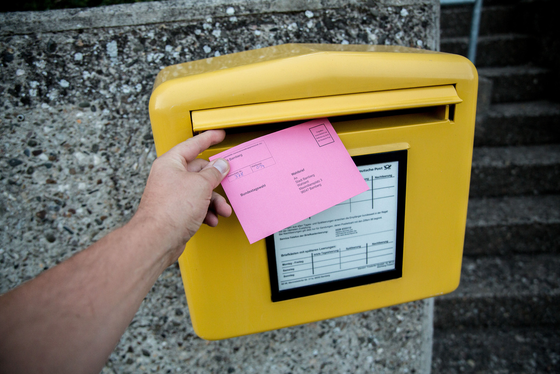 Hand steckt Wahlbriefumschlag in Postkasten
