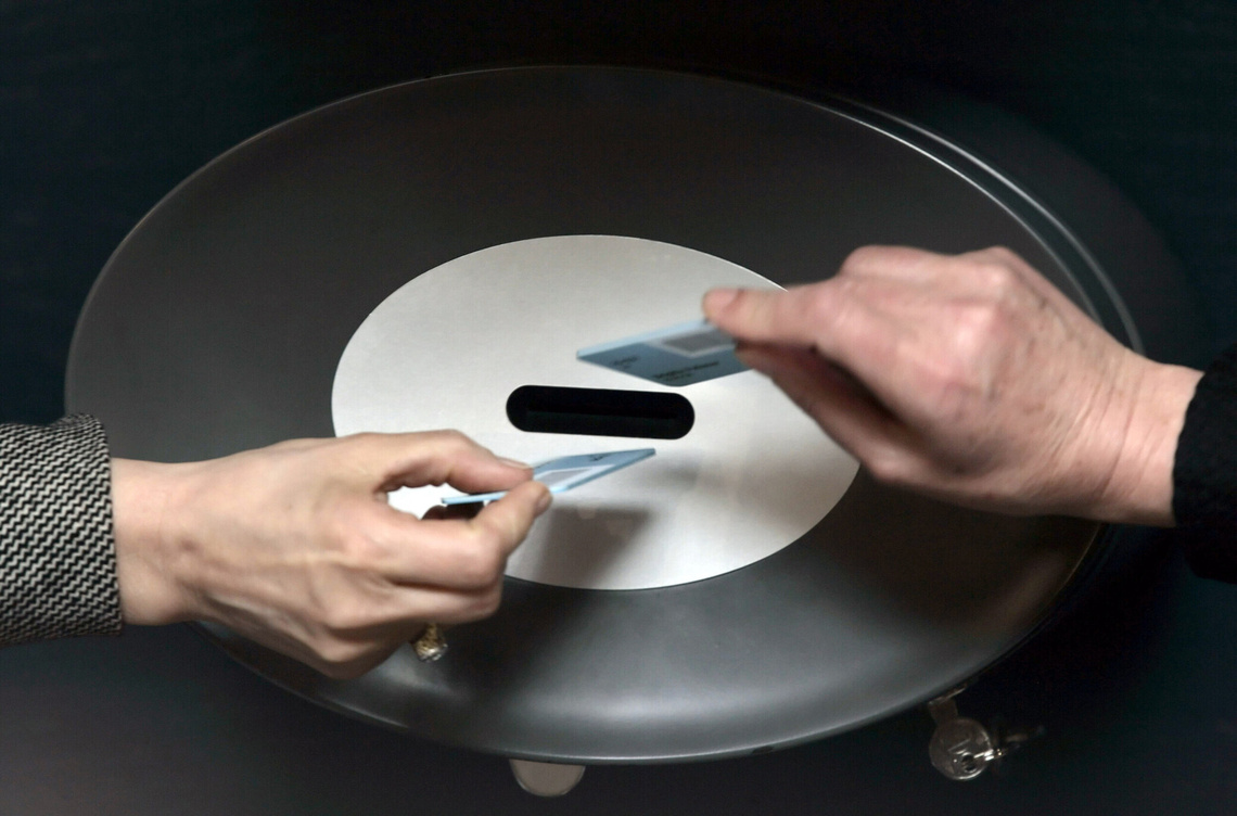 Zwei Hände stecken Stimmkarten in Wahlurnen