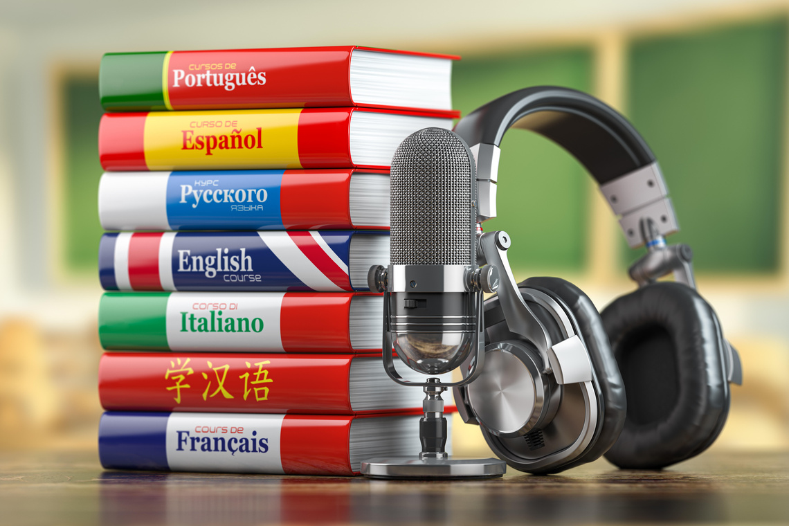 Neben einem Stapel bunter Wörterbücher verschiedener Sprachen sind ein Studio-Mikrofon und Kopfhörer zu sehen.