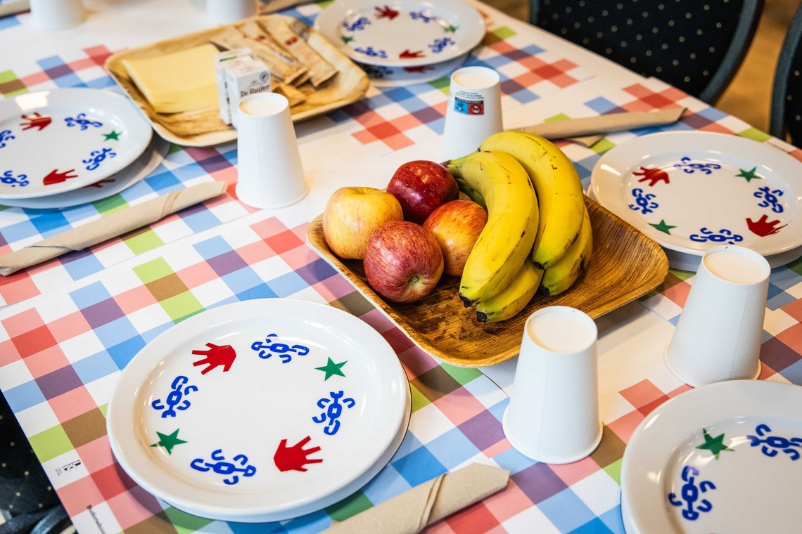 Ein Tisch mit karierter Tischdecke, gedeckt mit Tellern und Bechern. Auf dem Teller steht Obst.