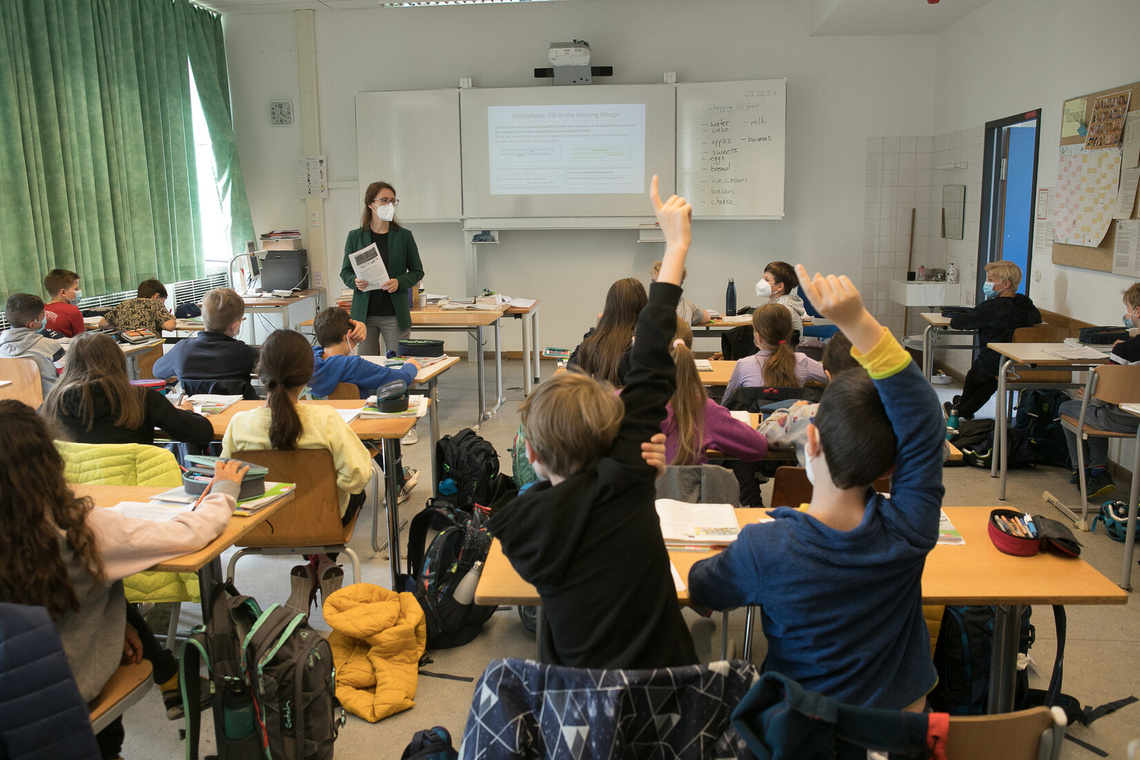 Klassenzimmer mit Kindern und Lehrerin, sie tragen Schutzmasken