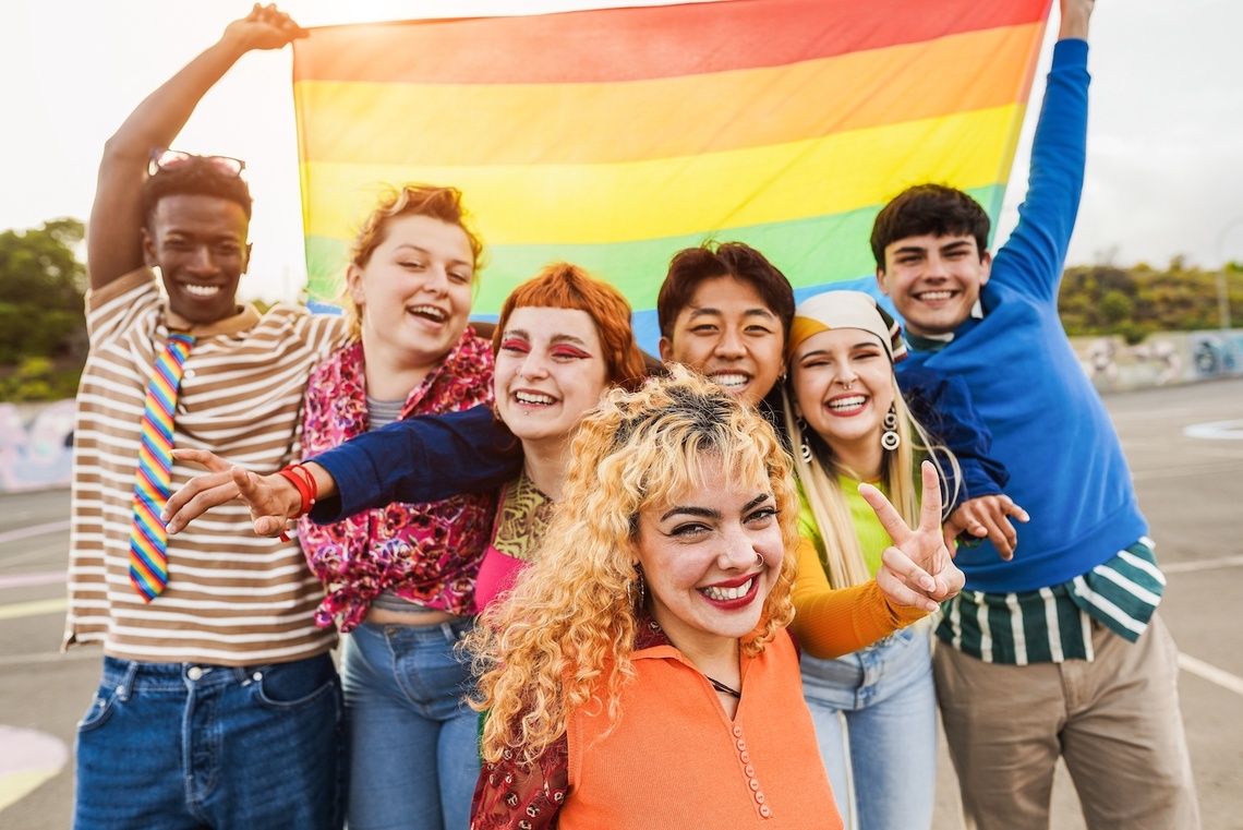 Lachende Jugendliche vor der regenbogenfarbigen LBGTQ-Flagge