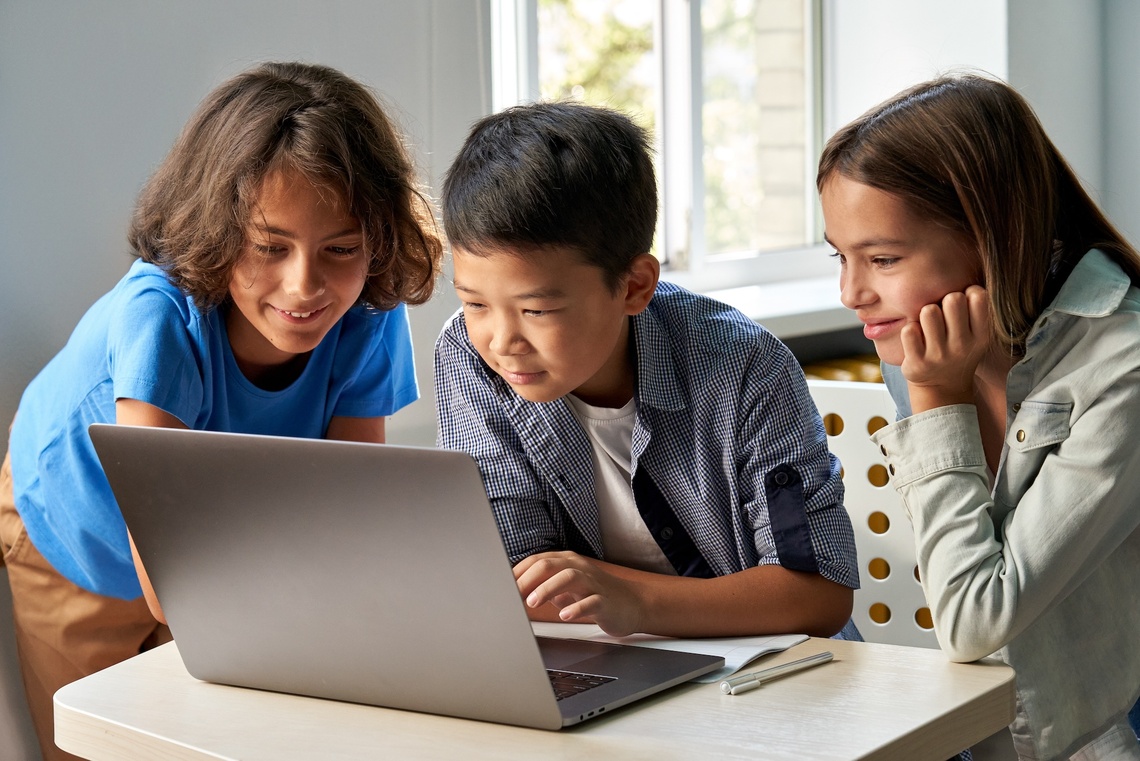 Drei Kinder sitzen an einem Tisch vor einem Laptop.