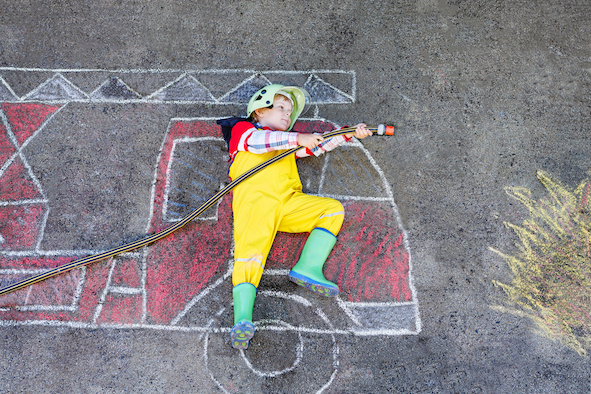 Junge in Feuerwehruniform, der Spaß mit Feuerwagen-Bild aus farbiget Kreide auf dem Asphalt hat
