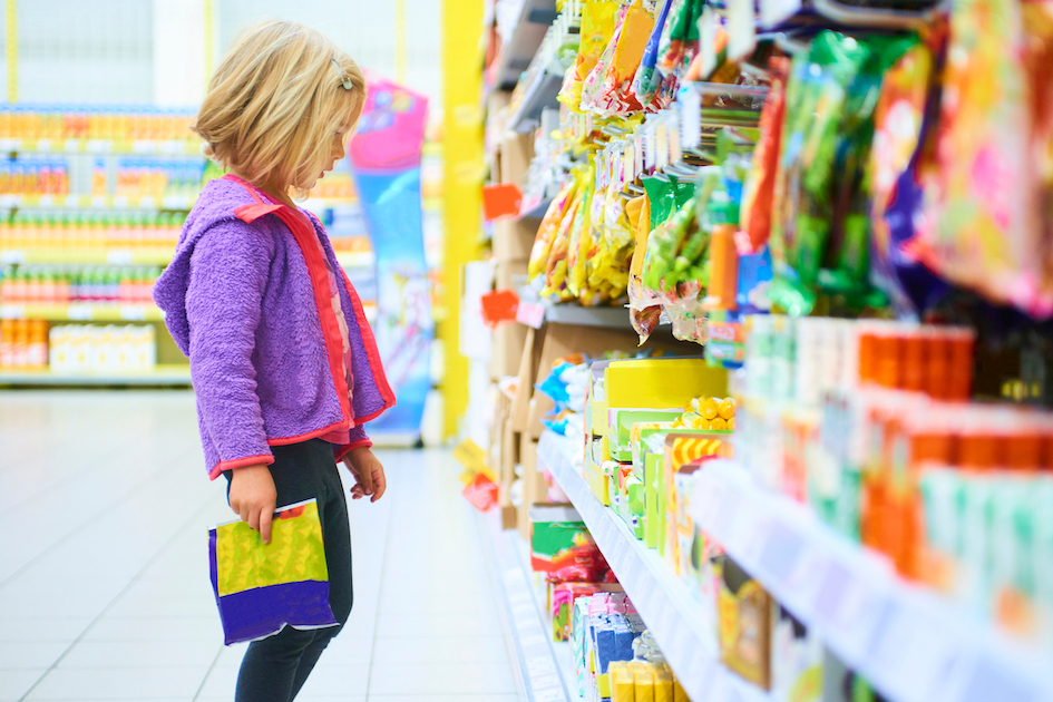 Mädchen steht vor dem Süßigkeitenregal im Supermarkt