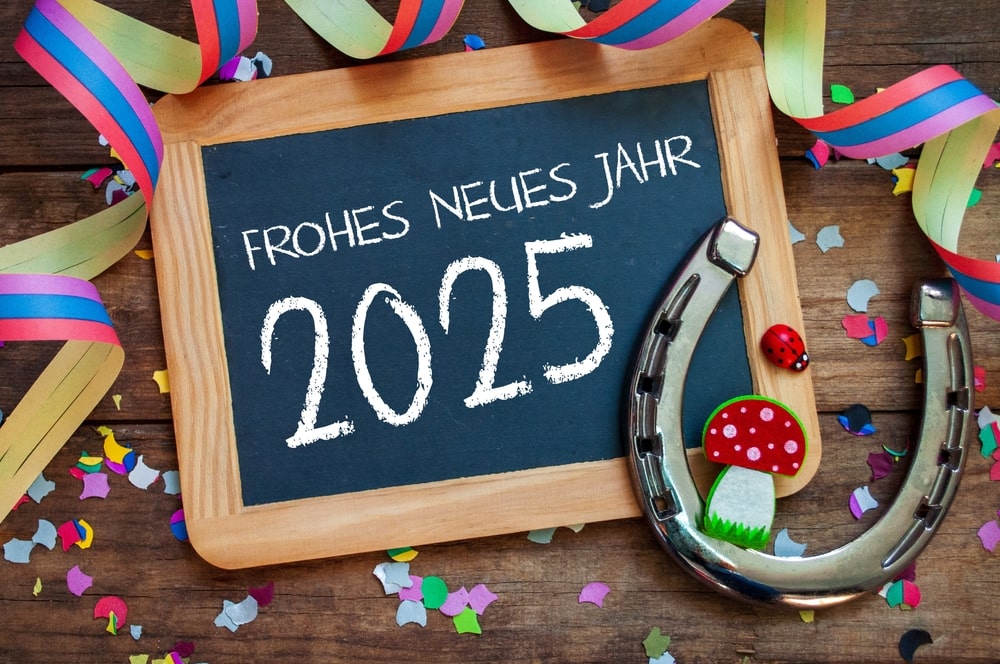 Eine kleine Tafel mit Holzrahmen liegt auf einem Holztisch. Auf der Tafel steht „Frohes neues Jahr 2025“.