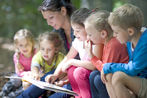Frau liest ein Buch vor einer Gruppe von Kindern vor.