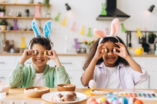 Zwei Kinder mit Osterhasen-Ohren halten sich Eier vor ihr Gesicht
