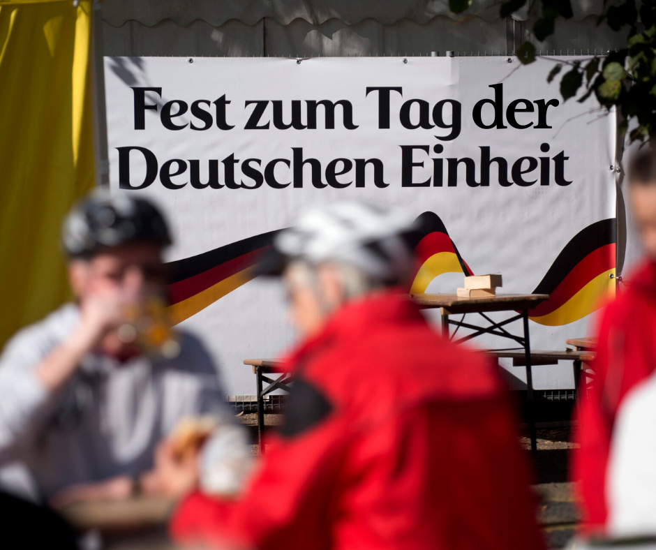 Banner mit Fest zum Tag der Deutschen Einheit, davor Menschen verschwommen