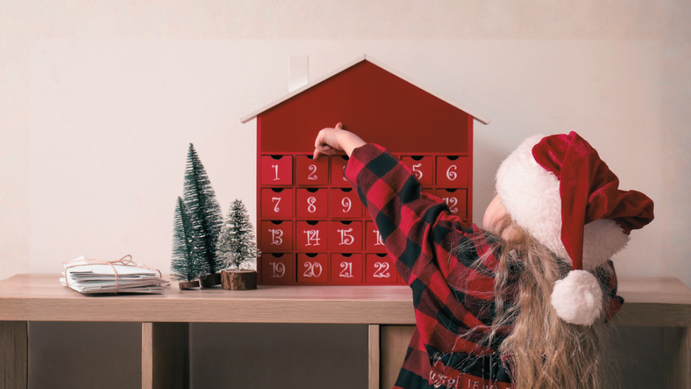 Mädchen mit Weihnachtsmütze vor hausförmigem, roten Adventskalender