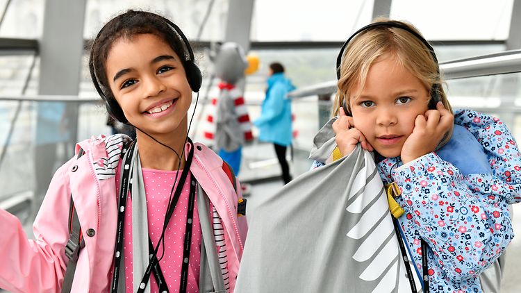 Zwei Kinder mit Kopfhörern in der Reichstagskuppel lachen in die Kamera